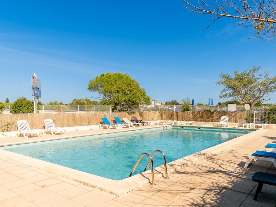 Outdoor pool with sun loungers at The Originals Hotels