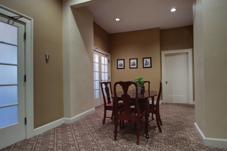 Dining area with four wooden chairs around a round table on patterned carpet in The Juneau Room at Knickerbocker On The Lake