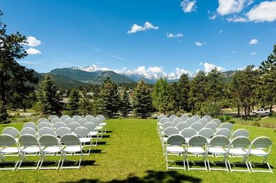 An outdoor wedding ceremony setup at The Stanley Hotel, with rows of white chairs facing a stunning mountain backdrop