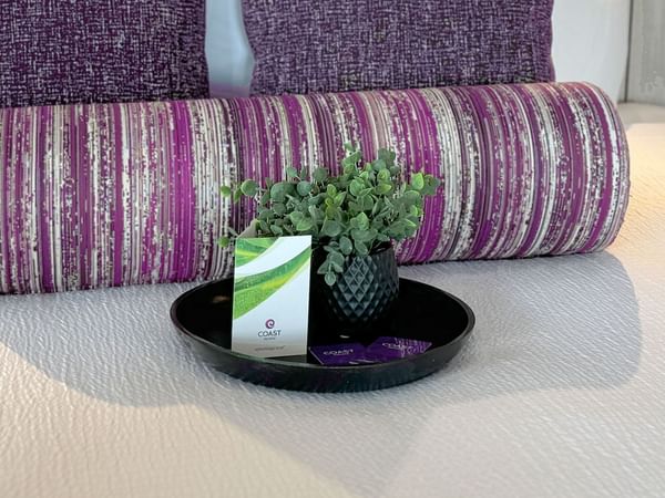 A bed with purple pillow and a tray holding a plant and a Coast Hotels room key.