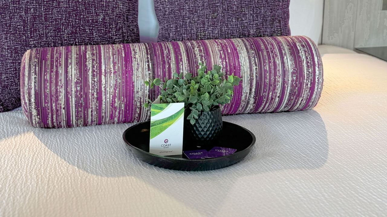 A bed with purple pillow and a tray holding a plant and a Coast Hotels room key.