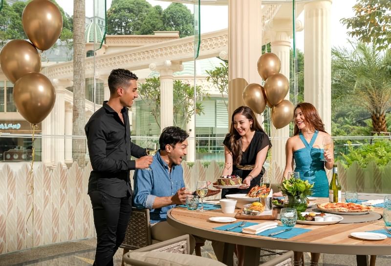 Outdoor birthday party with friends enjoying cake and wine, beautifully adorned with golden balloons at Sunway Resort
