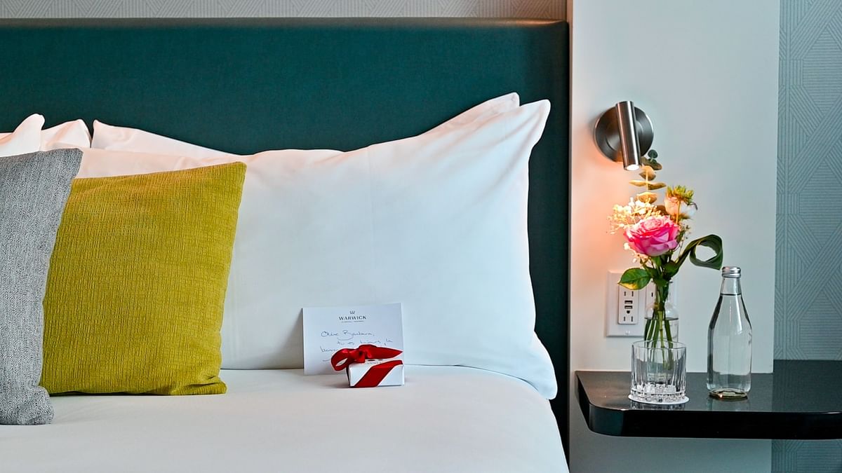 Bed with white linens, yellow pillow, flowers, and a gift at Warwick Corporate