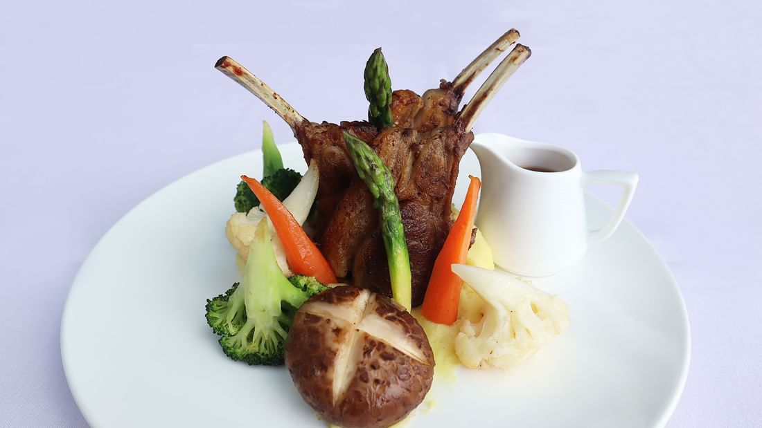 Grilled lamb chops with vegetables and a side of sauce on a white plate served in Pendas Cafe at Sunway Hotel Big Box