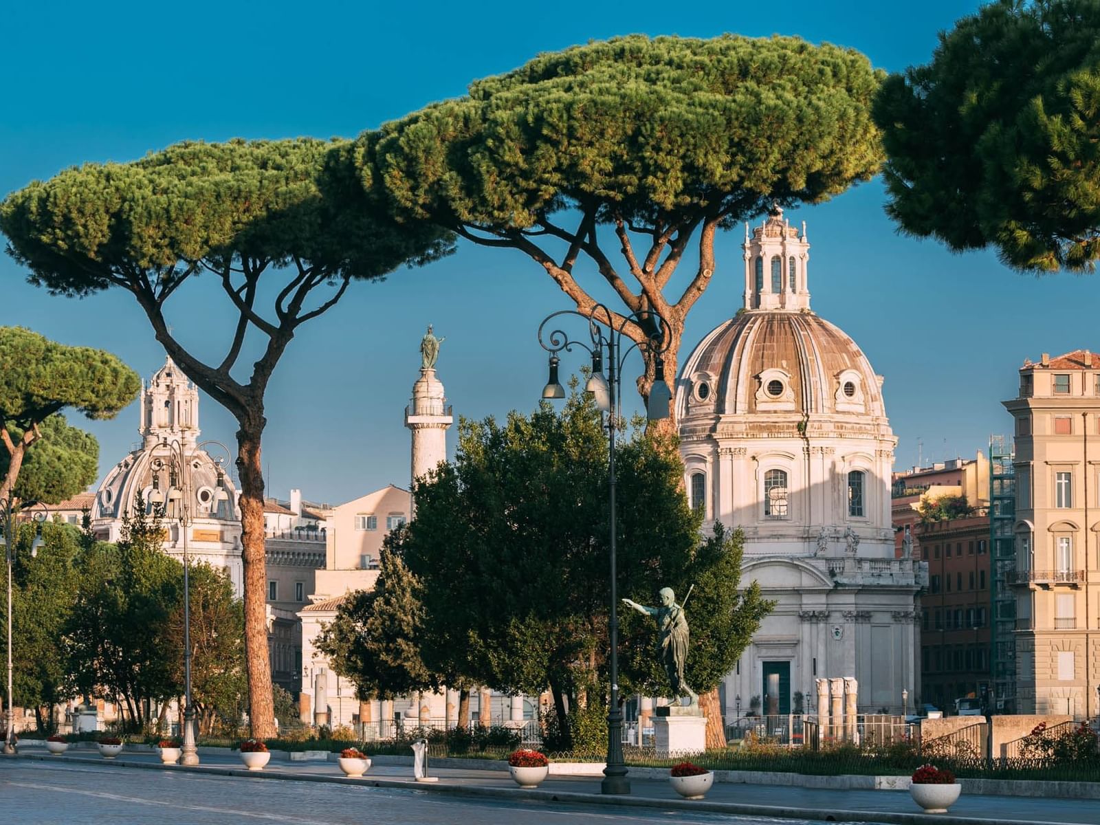 Trajan's Forum framed by tall pines, with ornate domes and sculptures near The Glam Hotel