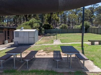 Picnic tables and benches under a shade sail in a grassy courtyard area.