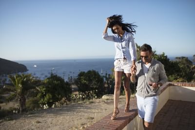 A couple walk holding hands on a pony wall and sea view at Banning House Lodge