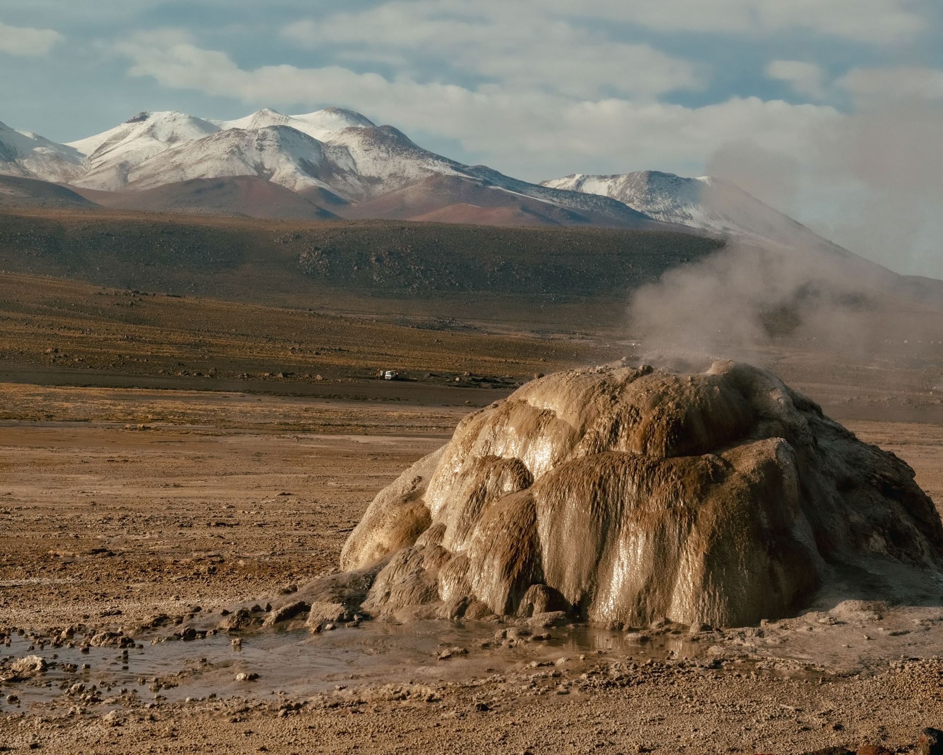 Géiser activo con vapor emergente en paisaje desértico con montañas nevadas al fondo en Cumbres San Pedro