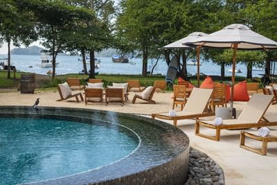 A tranquil poolside setting with sun loungers near a beach at El Mangroove Hotel