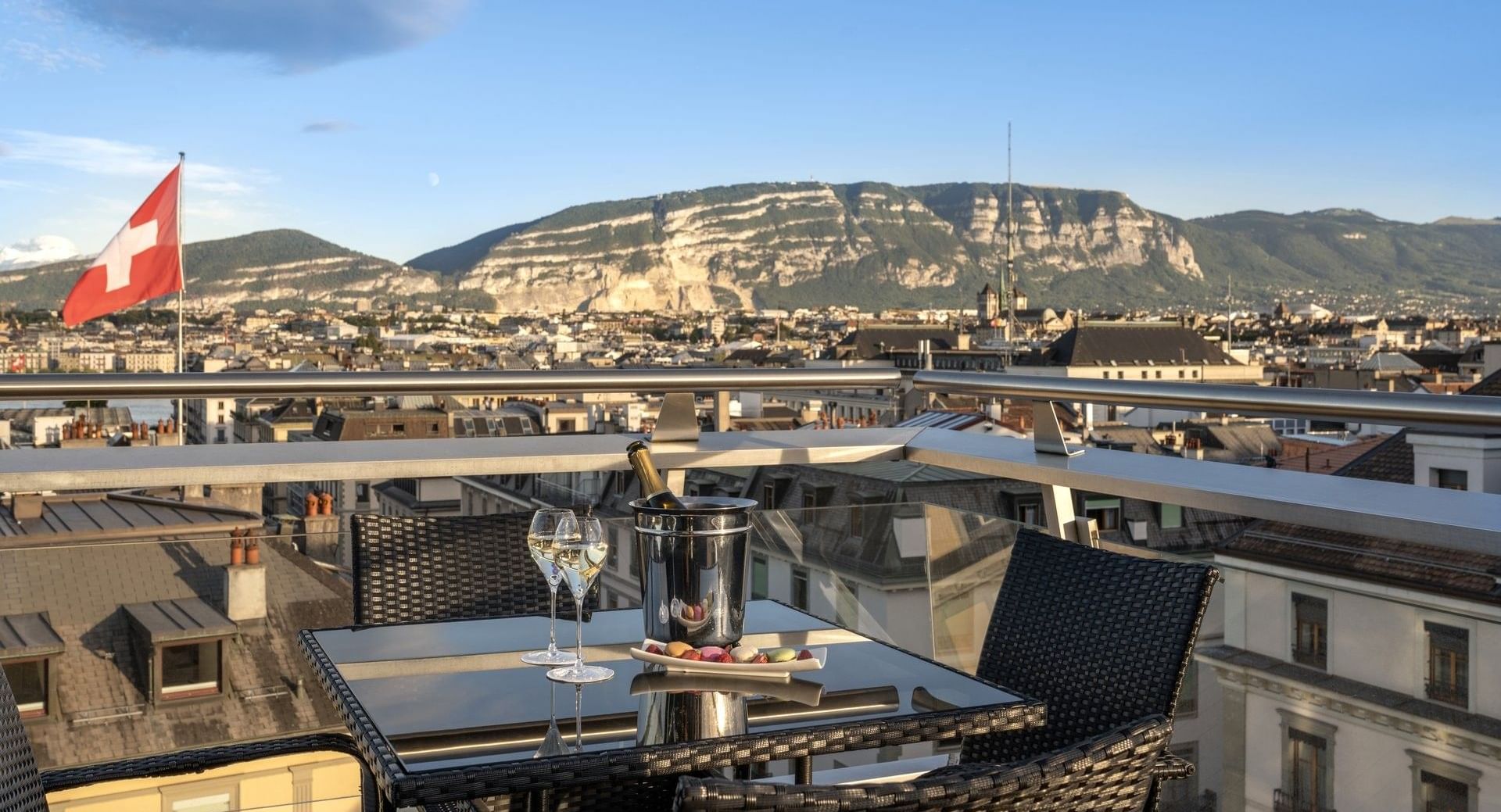 Bistro set by a railing under a blue sky surrounding a mountain in Penthouse Terrace Suite at Warwick Geneva