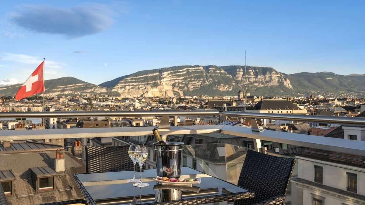 Rooftop terrace with a glass table, nestled among chairs and a wine bucket in Penthouse Terrace Room at Warwick Geneva