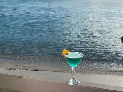 Teal tropical cocktail garnished with a starfruit slice resting on a ledge by the sea at Emerald Beach Resort