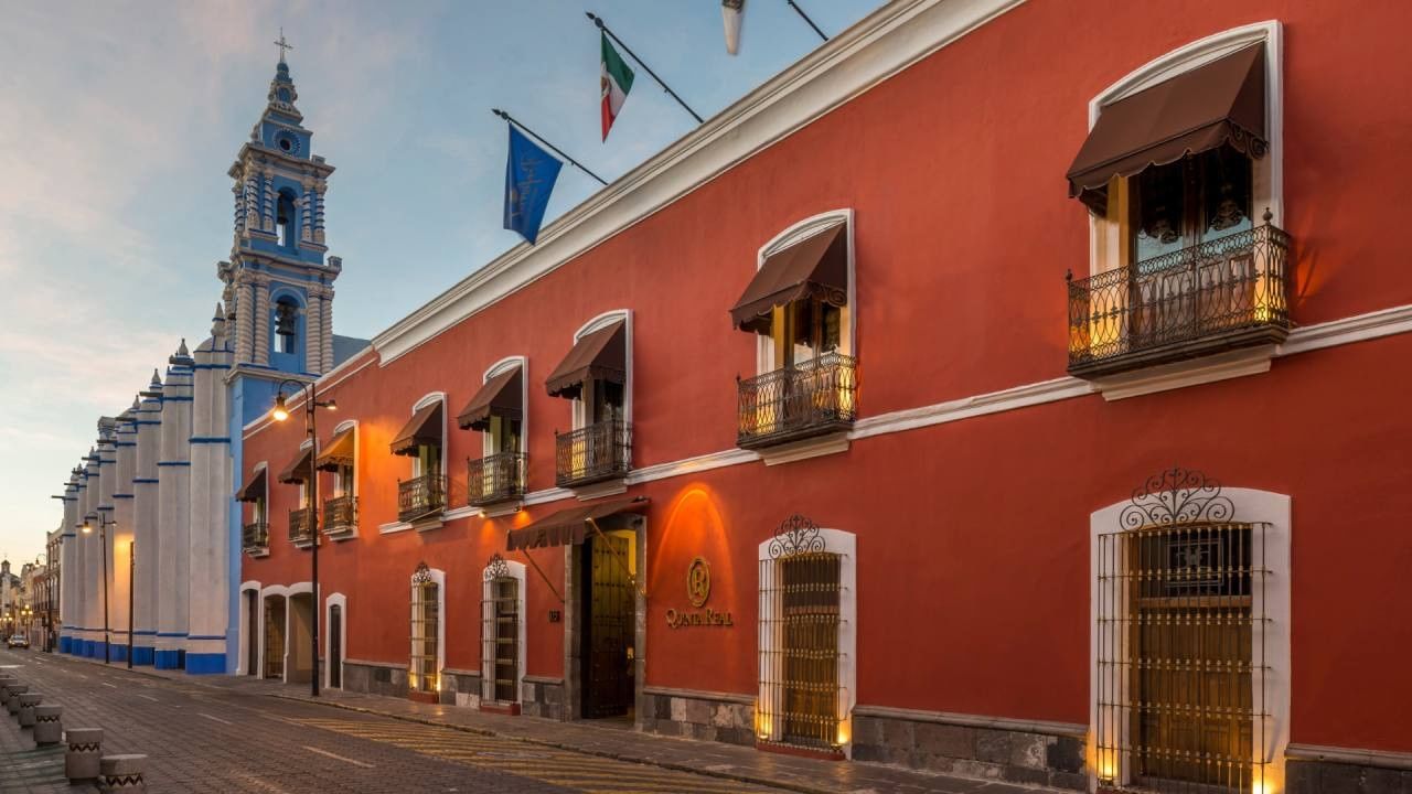 Red building by a blue tower under a soft sky surrounding the street at Camino Real Pedregal Mexico