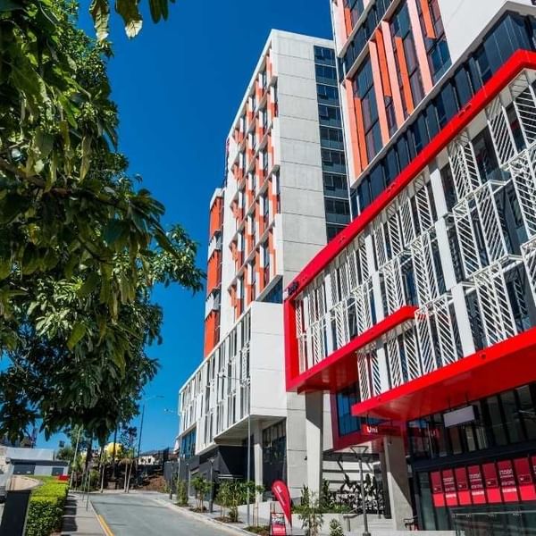 Modern urban building in Brisbane with red and white facade, glass windows, and adjacent greenery.