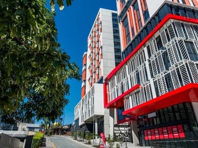 Modern urban building in Brisbane with red and white facade, glass windows, and adjacent greenery.