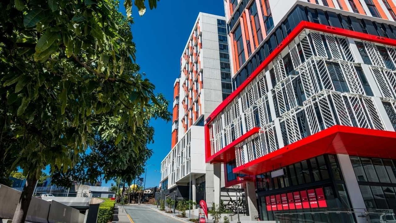 Modern urban building in Brisbane with red and white facade, glass windows, and adjacent greenery.
