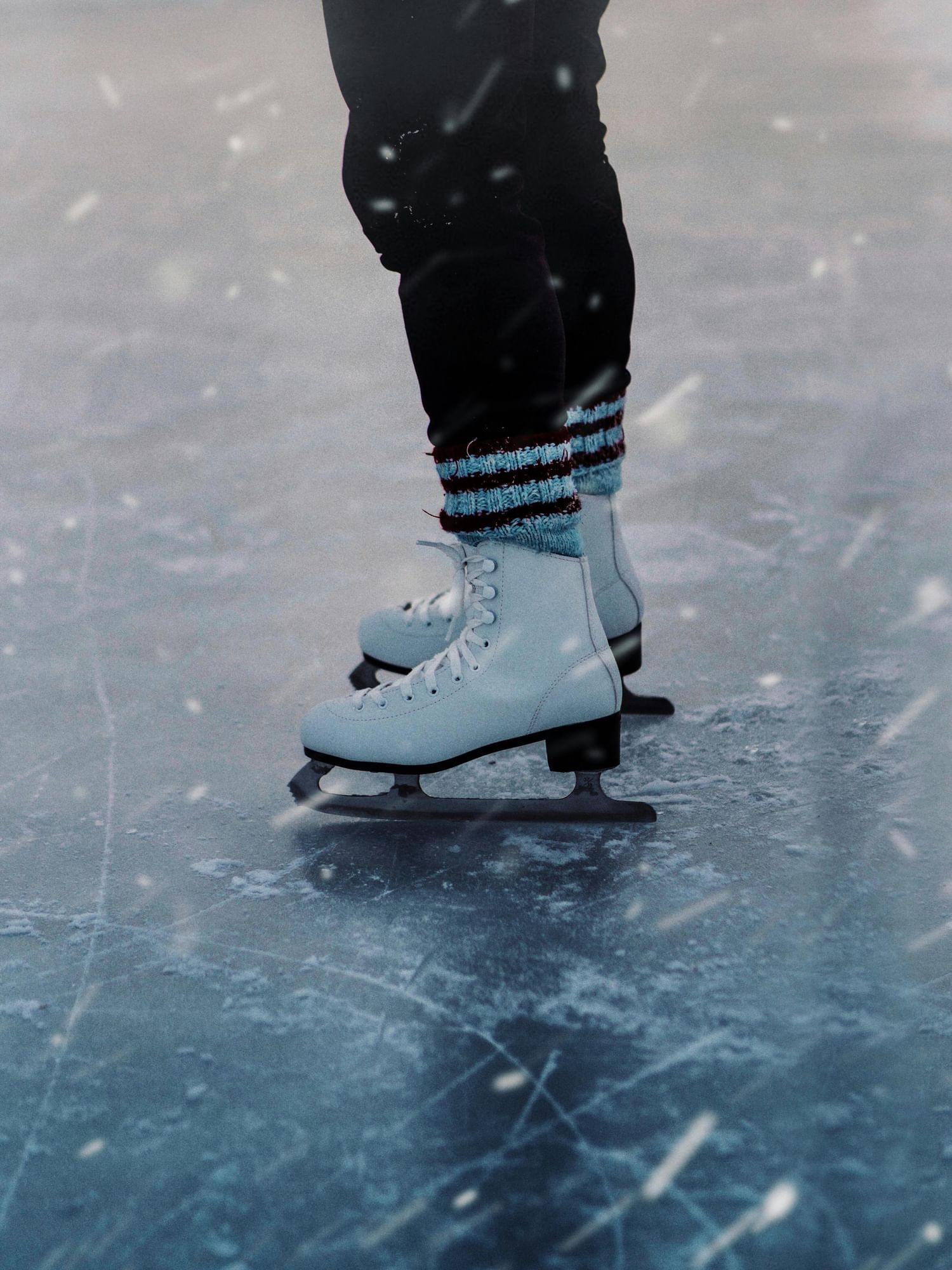 Legs in black pants and white ice skates on the ice. Try ice skating at Now Snowing in Celebration.