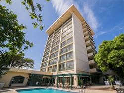 Exterior view of Courtleigh Hotel & Suites surrounded by trees by a pool, one of the best hotels in Kingston, Jamaica