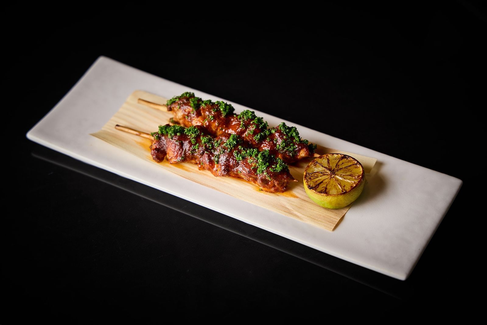 Brochettes de viande grillées, garnies d'herbes aromatiques et d'un demi-citron grillé, servies sur une planche en bois au restaurant The Londoner