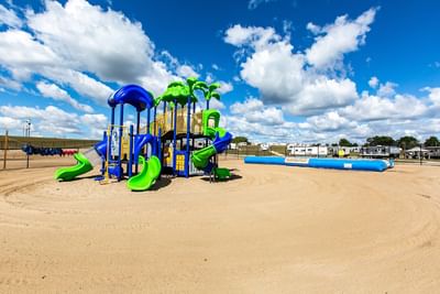 Playground with blue and green slides and jumping pad, surrounded by sandy area at Off Shore Resort