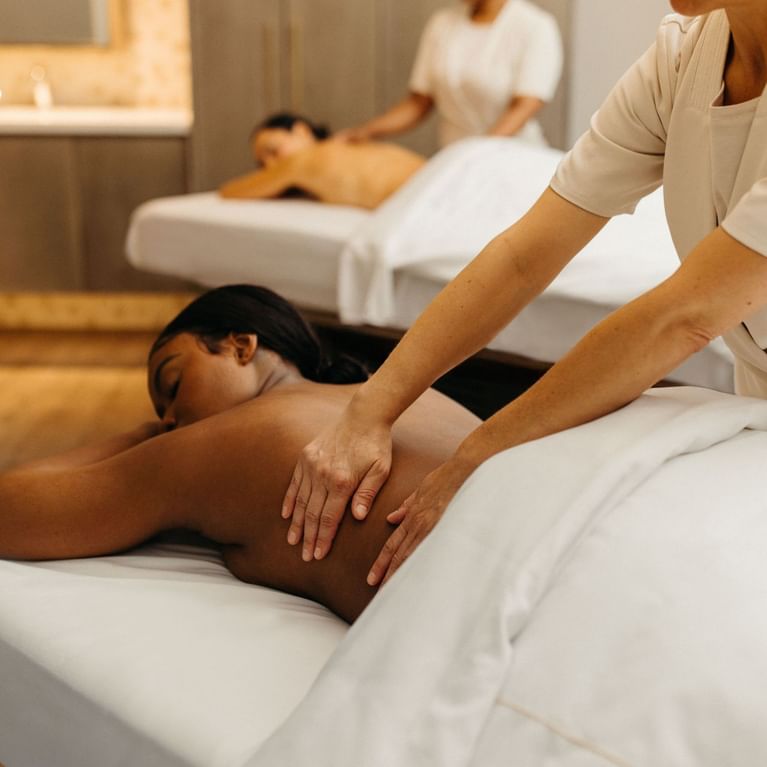 Therapist massaging a guest\'s back on a white treatment bed by a second bed in Guerlain Spa at Hotel X Toronto