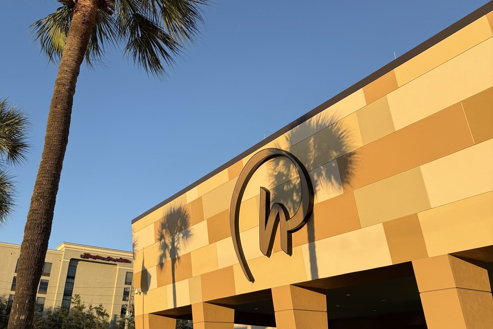 A close-up of the Rosen Hotels logo on the front of Rosen Inn International with the shadows of palm trees at sunset.