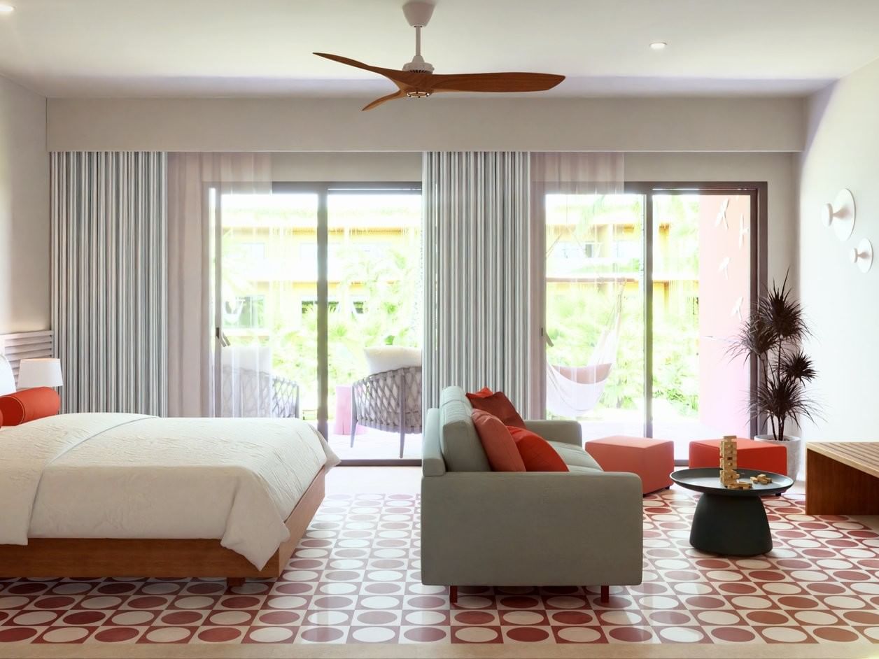 Junior Suite Pool Level espaciosa con sofá gris y balcón tropical en Fiesta Americana Funeeq Punta Cana