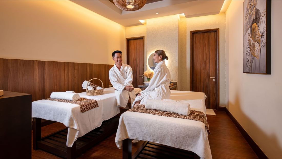 Happy couple in white robes sitting on massage beds in a spa treatment room at Sunway Resort