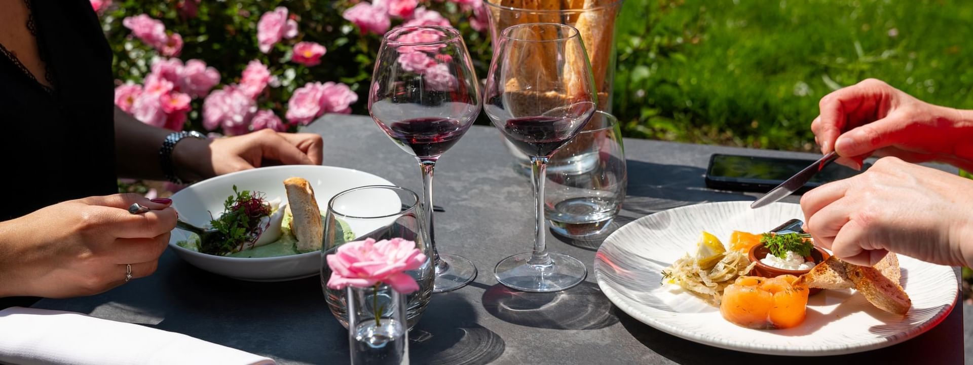 Scène de dîner en plein air mettant en scène deux personnes savourant un repas et du vin rouge chez Warwick Hotels and Resorts, avec des roses roses