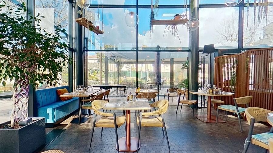 Vue intérieure d'un restaurant avec mobilier en bois et canapés bleus, sous une verrière lumineuse.