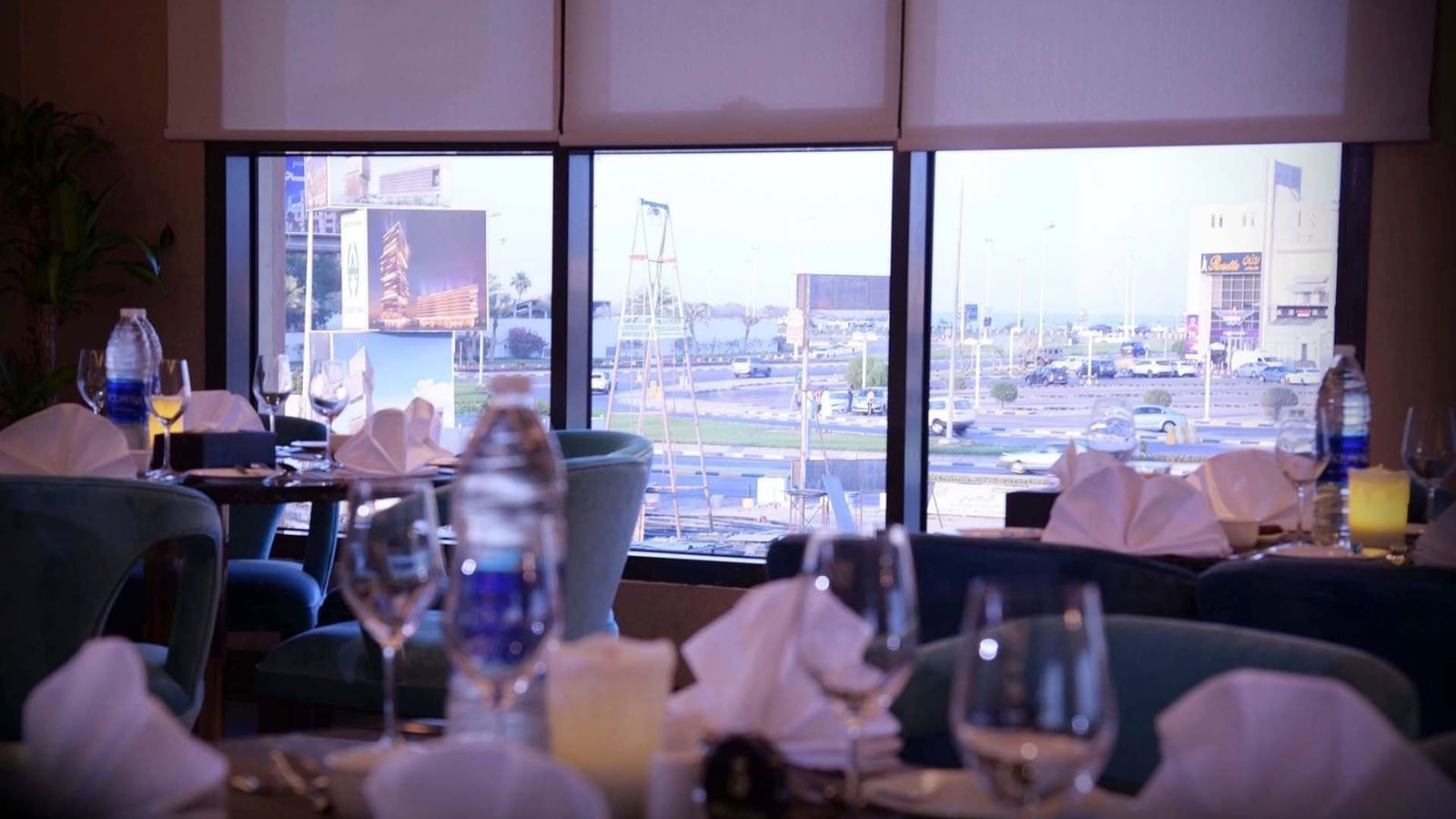 Dining tables with white linens by large windows in Al Multaqa Restaurant at Warwick Al Khobar