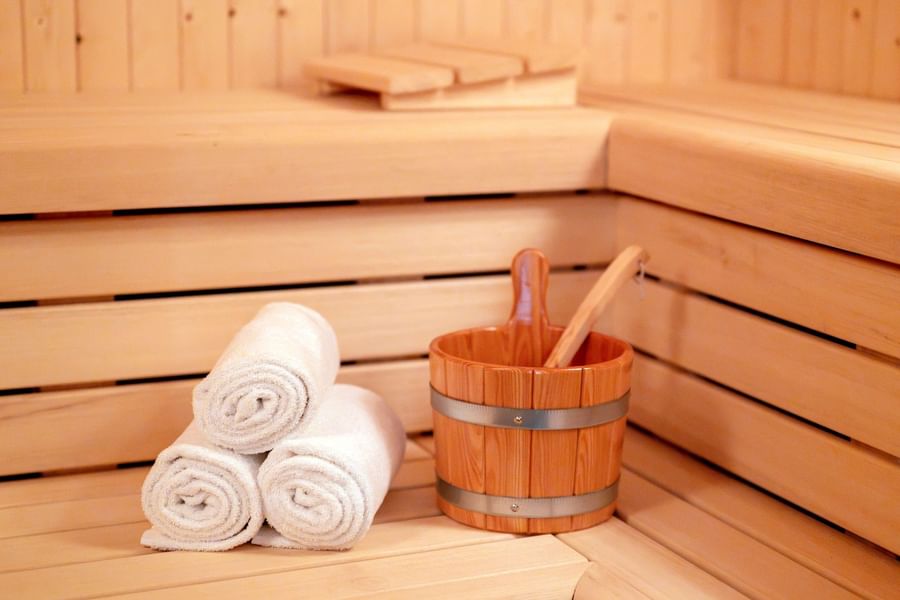 Wooden sauna interior with rolled white towels and wooden bucket with ladle at Warwick Brussels Grand-Place