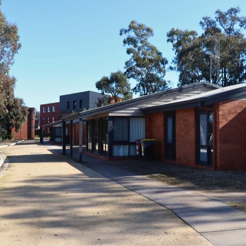 Row of brick buildings with a paved walkway and trees at La Trobe University Terraces.