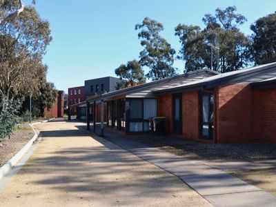 Row of brick buildings with a paved walkway and trees at La Trobe University Terraces.