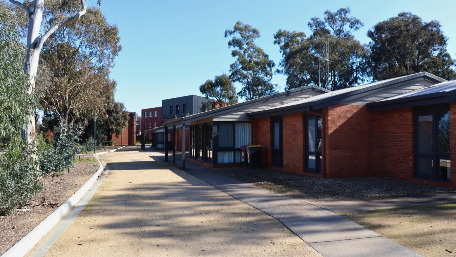 Row of brick buildings with a paved walkway and trees at La Trobe University Terraces.