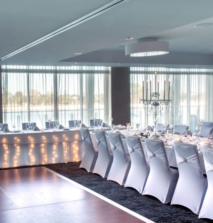 Wedding reception with long tables covered with white tablecloths and illuminated lights at The Sebel Mandurah