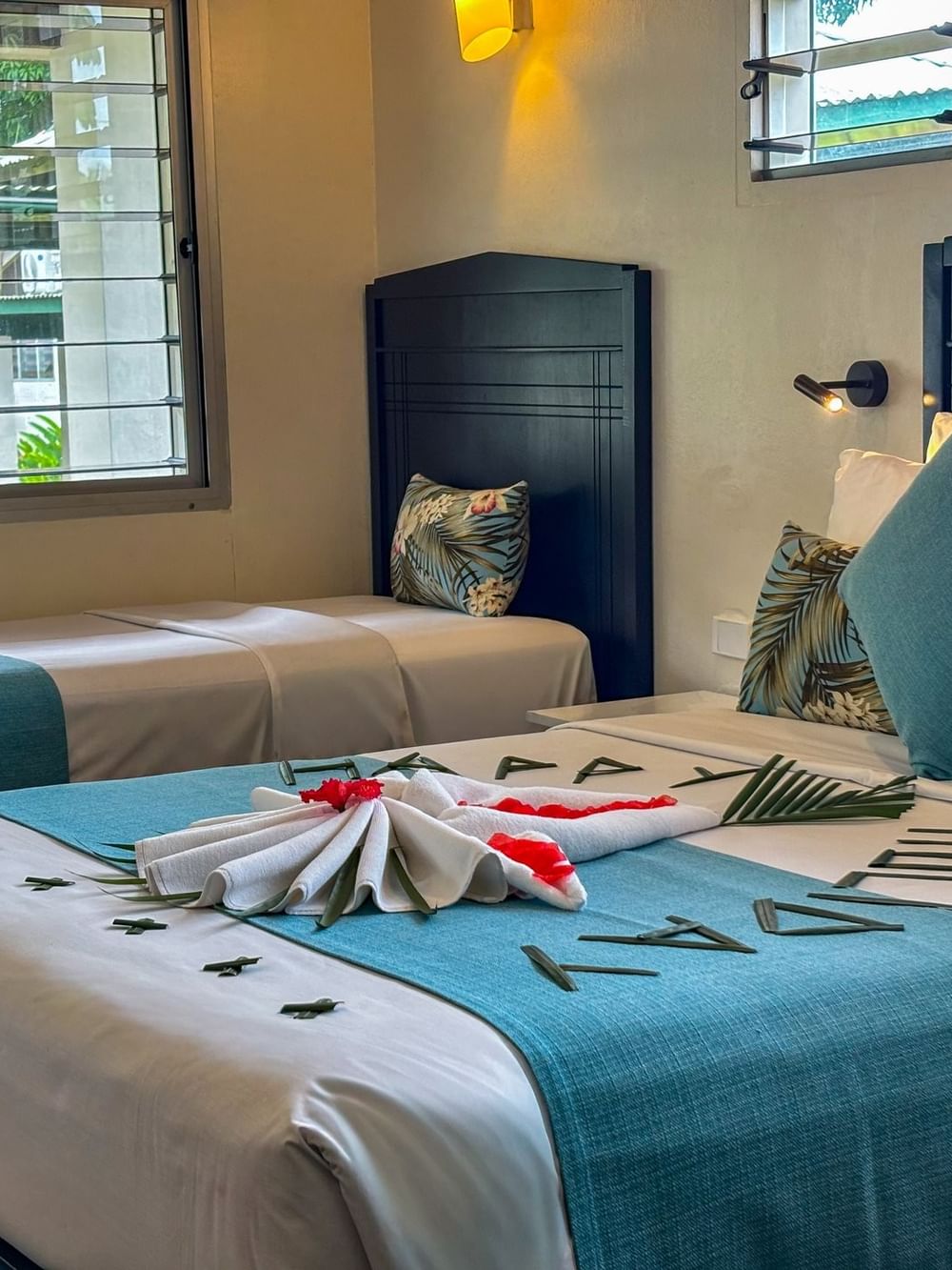 Beds with teal runners and leaf decorations by a window under a warm wall lamp in Family Room at TokaToka Resort Nadi Fiji