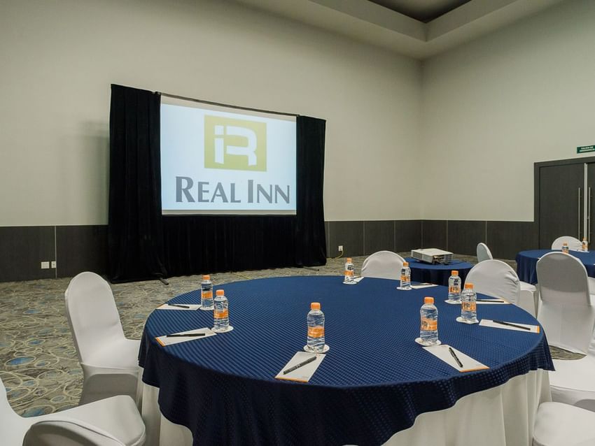 Banquet set-up with blue linens and a projector screen in the Verona Venue at Real Inn Tijuana