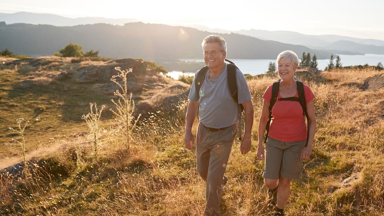 Two hikers with backpacks walking on a golden hillside trail in summer.
