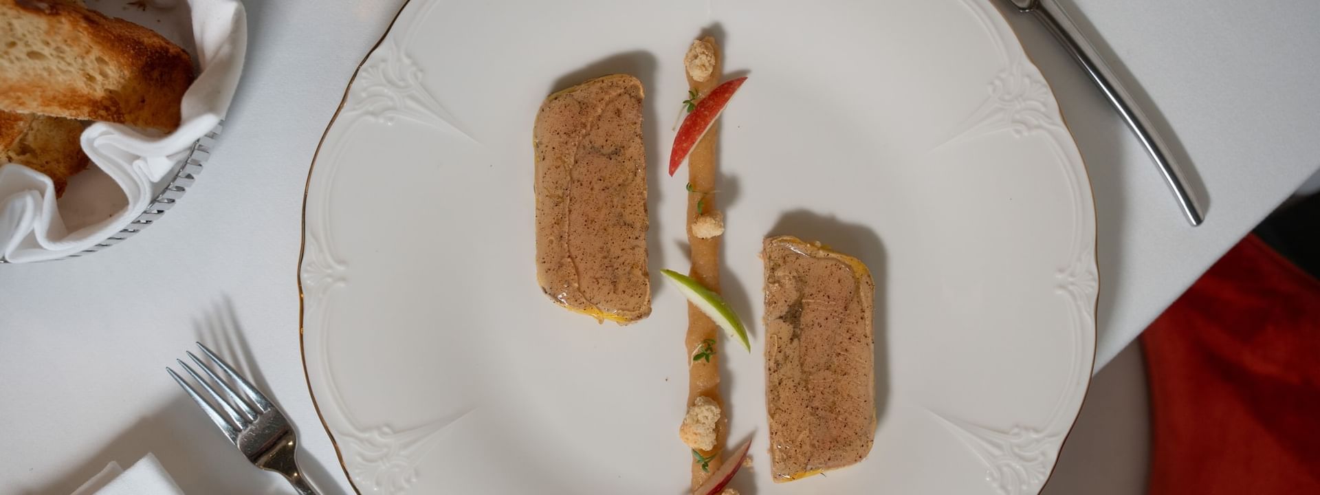 Gourmet pâté served with apple slices on a white plate placed with silver cutlery in Le Céladon at Hotel Westminster Paris