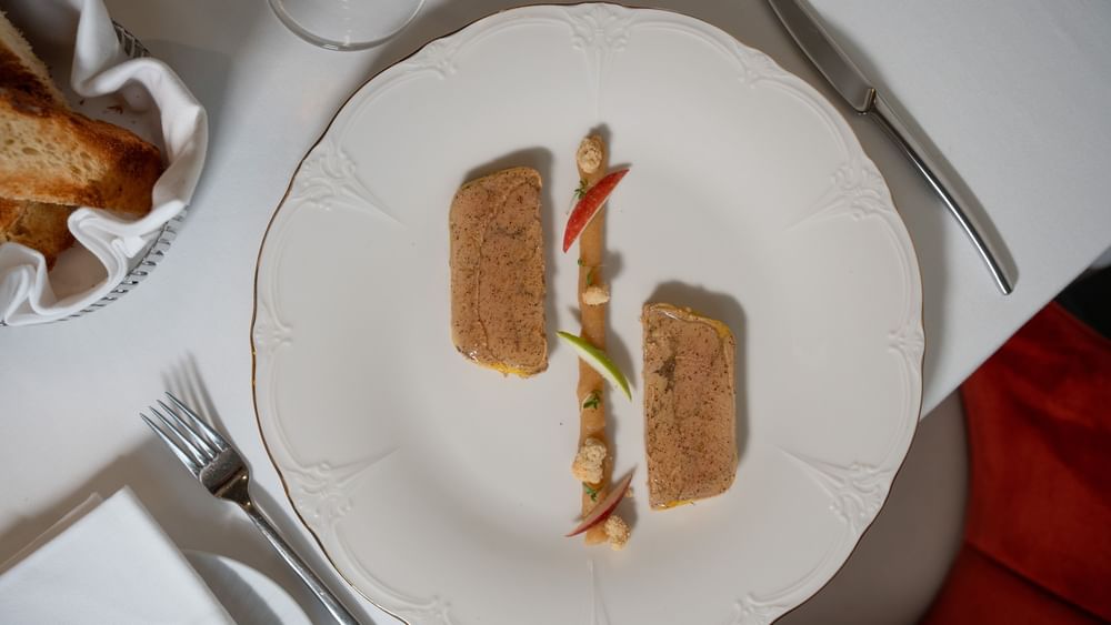 Gourmet pâté served with apple slices on a white plate placed with silver cutlery in Le Céladon at Hotel Westminster Paris