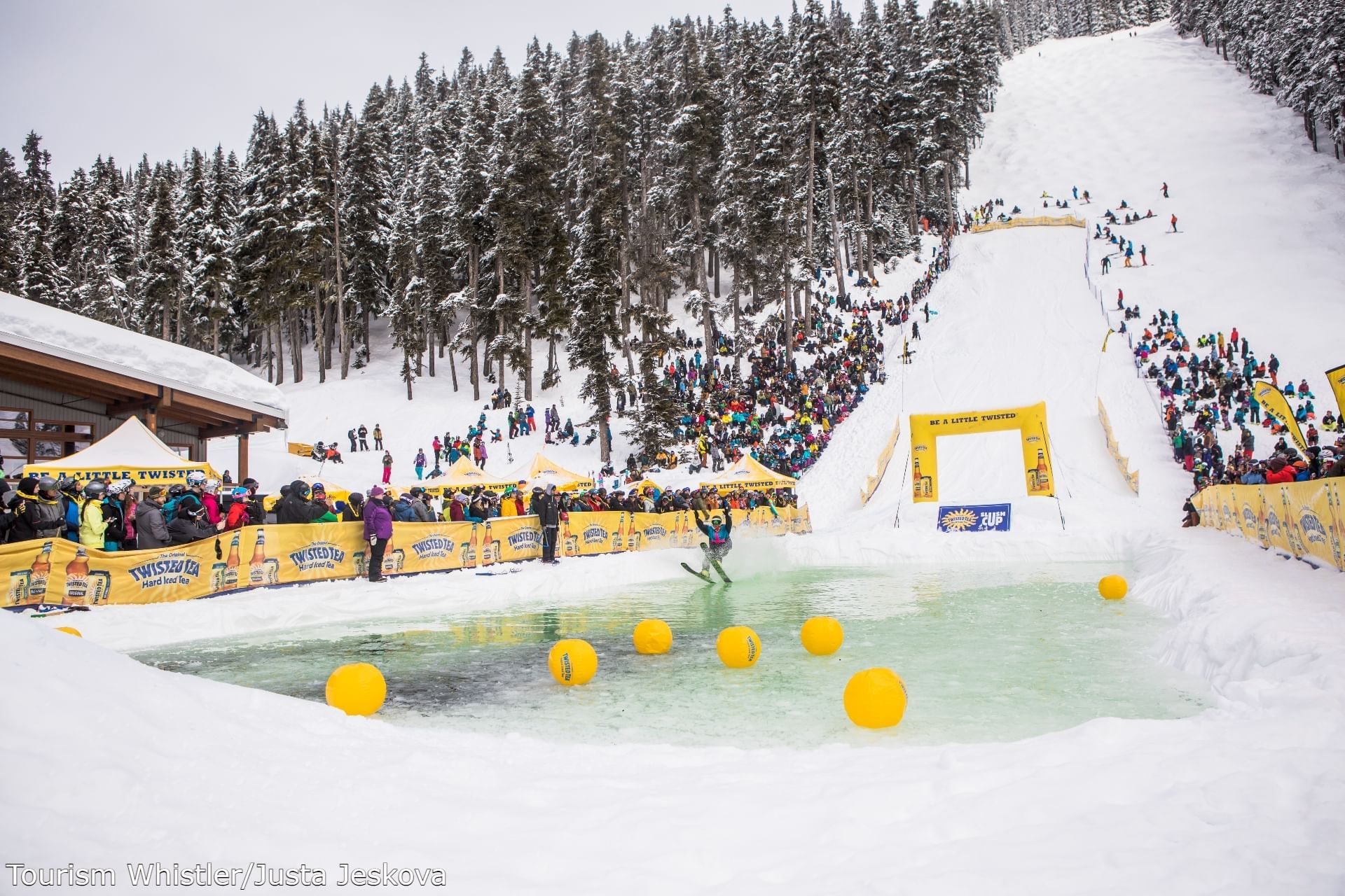 Crowded snowy pathway in Slush Cup event over an icy water pool near Blackcomb Springs Suites