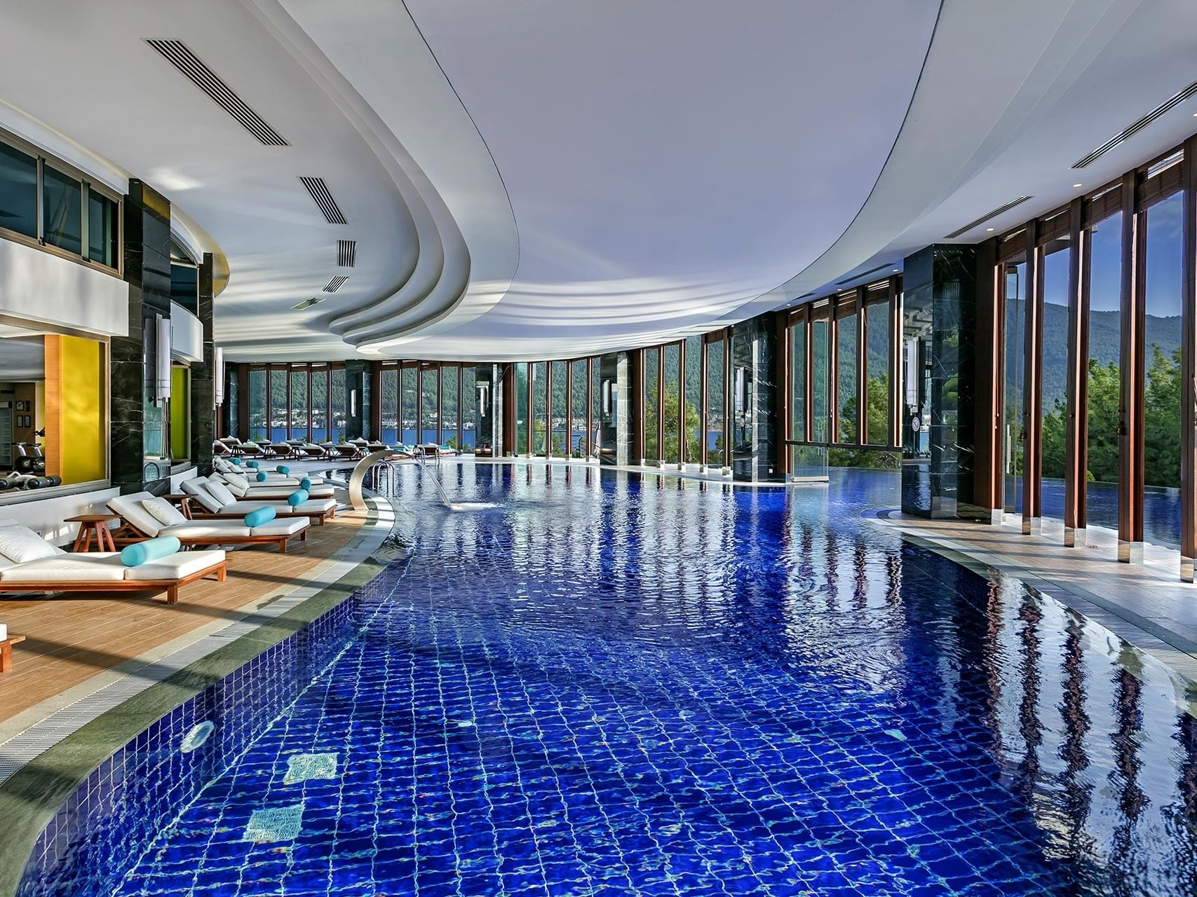 At Titanic Luxury Collection Bodrum, the indoor pool with glass walls and poolside loungers offers a serene retreat.