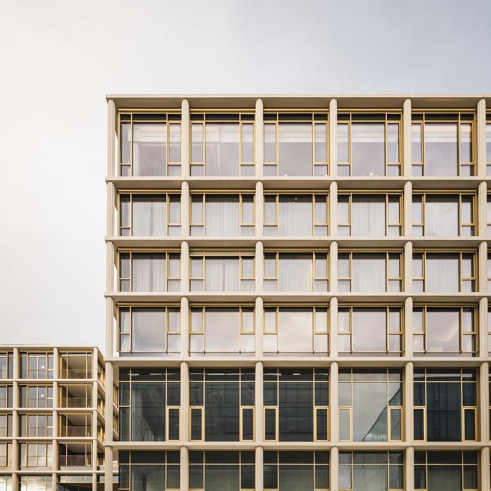 Edificio moderno con facciata in vetro e cornici dorate, finestre con tende bianche.