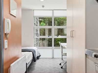 Modern student room with bed, desk, and kitchen area at Student Living Auckland Beach.