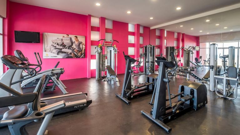 Spacious hotel gym with bright pink accent walls and a variety of workout machines at Camino Real Veracruz