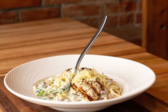 a fork stands upright in a bowl of chicken alfredo pasta