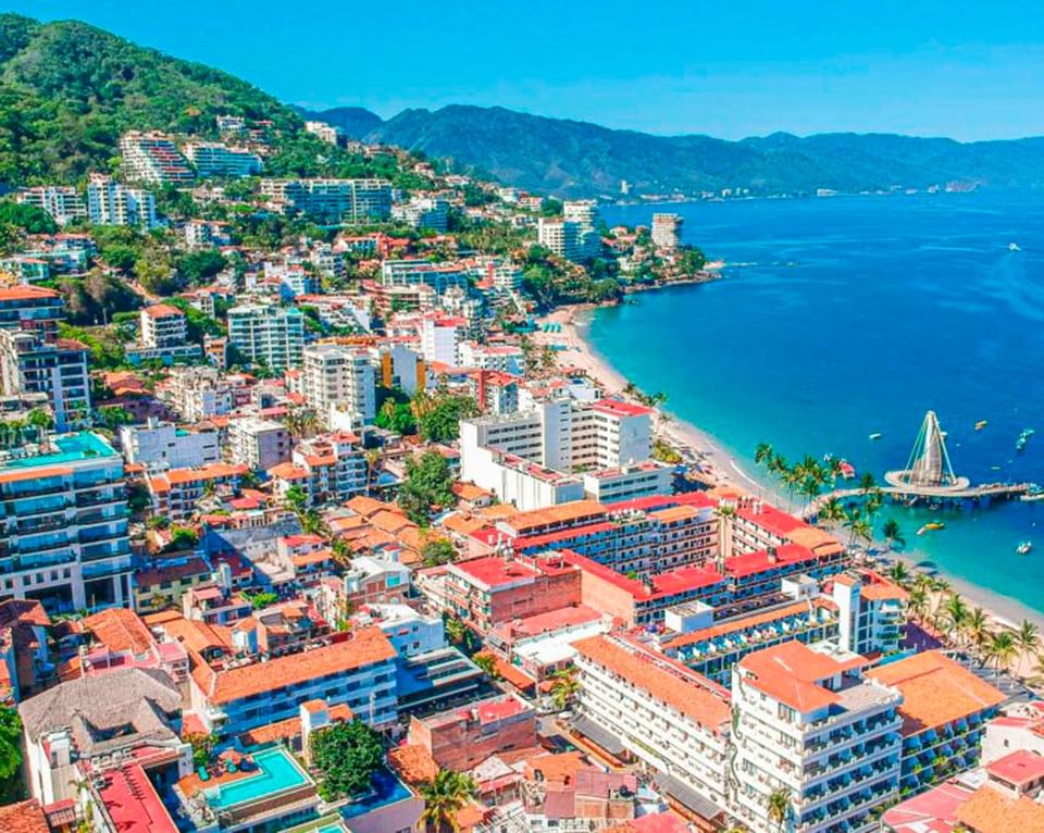 Aerial drone view of a coastal city with buildings along a sandy beach and blue ocean near Casa Dona Susana