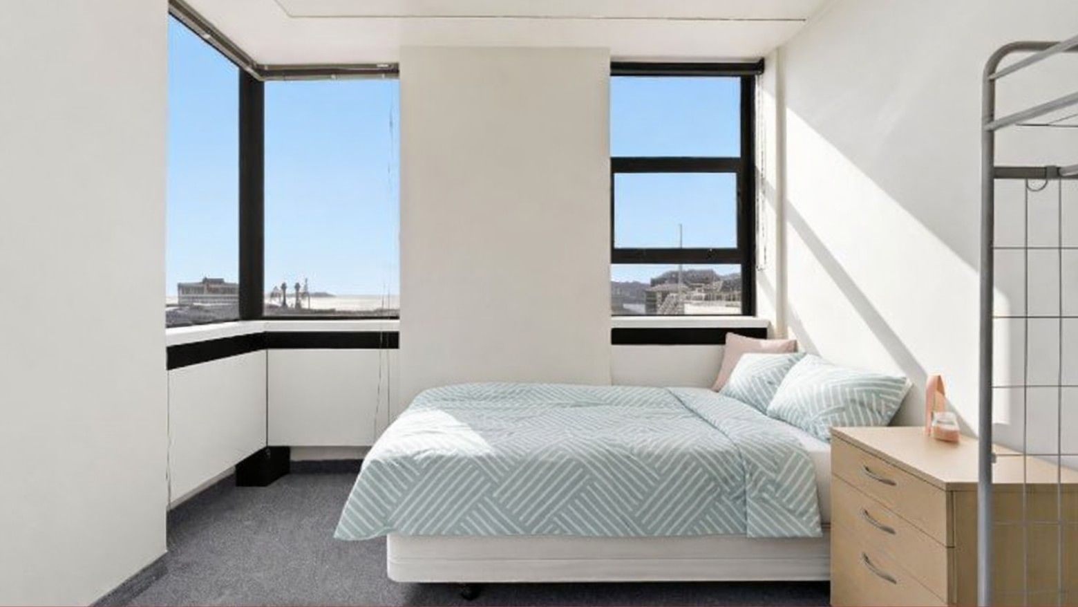 Clean, modern bedroom with bed, two windows, and a dresser at UniLodge Stafford House.