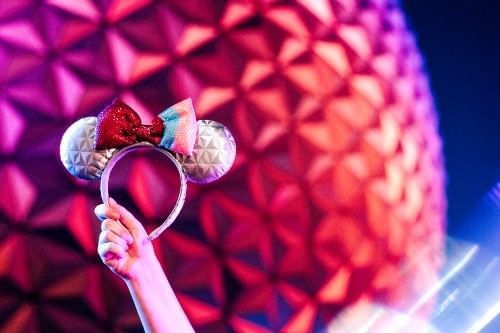 A guest holds up Minnie Mouse ears in front of Spaceship Earth at EPCOT, a theme park which just received new parking lot signs. 